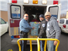 Police Officer and two other volunteers putting a box of toys into an ambulance