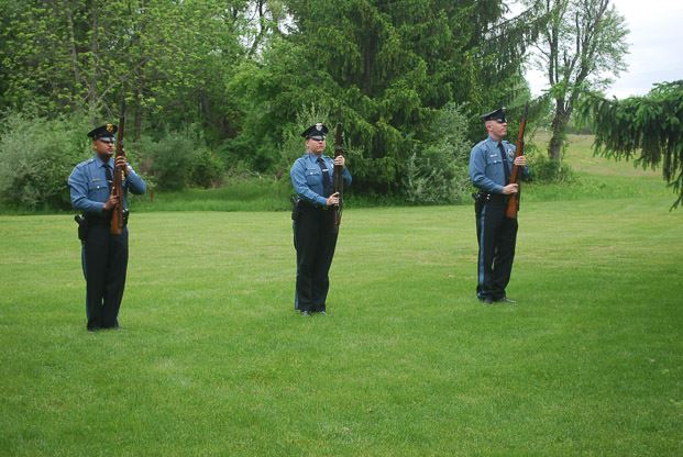 Three officers in uniform standing at attention with  rifles in hand in grass