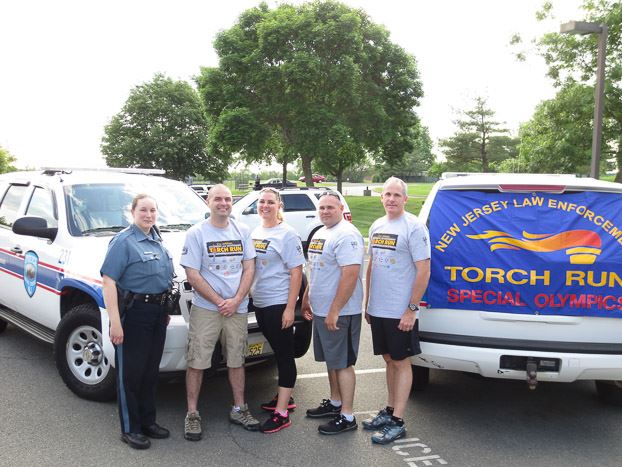 Five officers standing in front of a truck with torch Run sign on it
