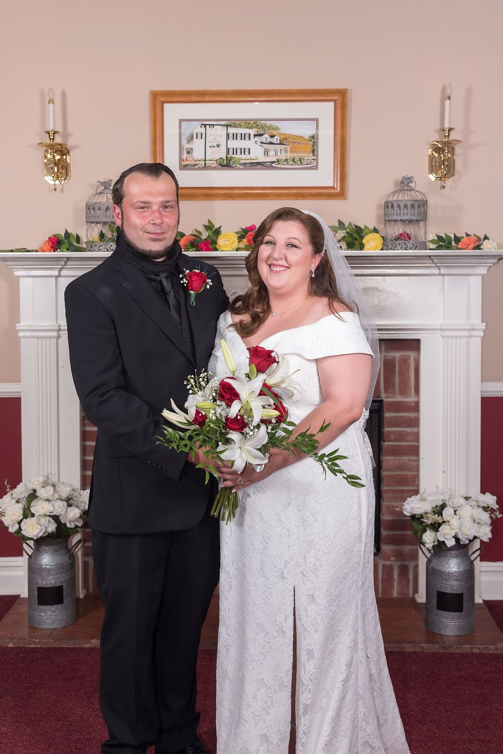 Kaitlin and her husband in wedding wear, standing in front of a fireplace